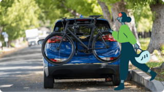A blue car with a bike as a person walks past on the sidewalk.