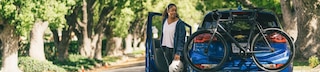 Woman exiting car and walking towards bike on rear of car