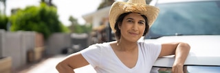 Woman in hat posing while leaning against vehicle
