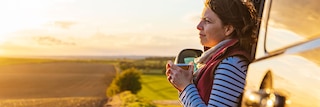 Woman leaning on vehicle starting into sunset